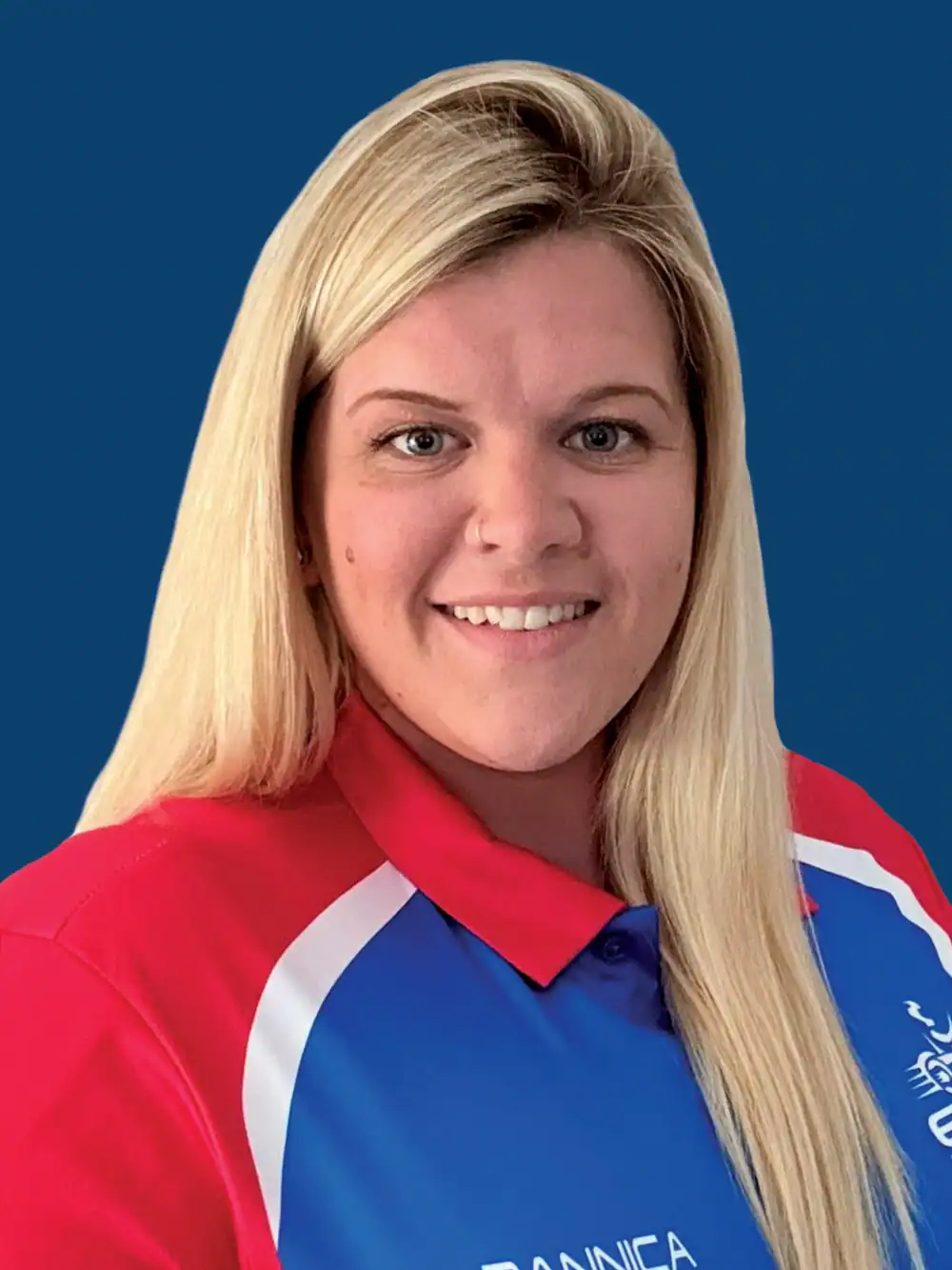 A woman with long blonde hair wearing a blue, red, and white collared shirt poses in front of a solid blue background, smiling at the camera.