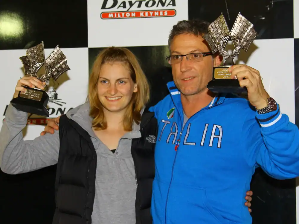 Two people stand side by side holding trophies, smiling at the camera, in front of a Daytona Milton Keynes backdrop.