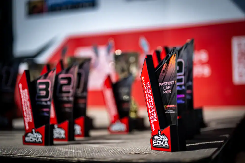 Close-up of several EDKA racing trophies arranged on a table, with awards for different categories including "Fastest Lap Men" visible in the foreground.