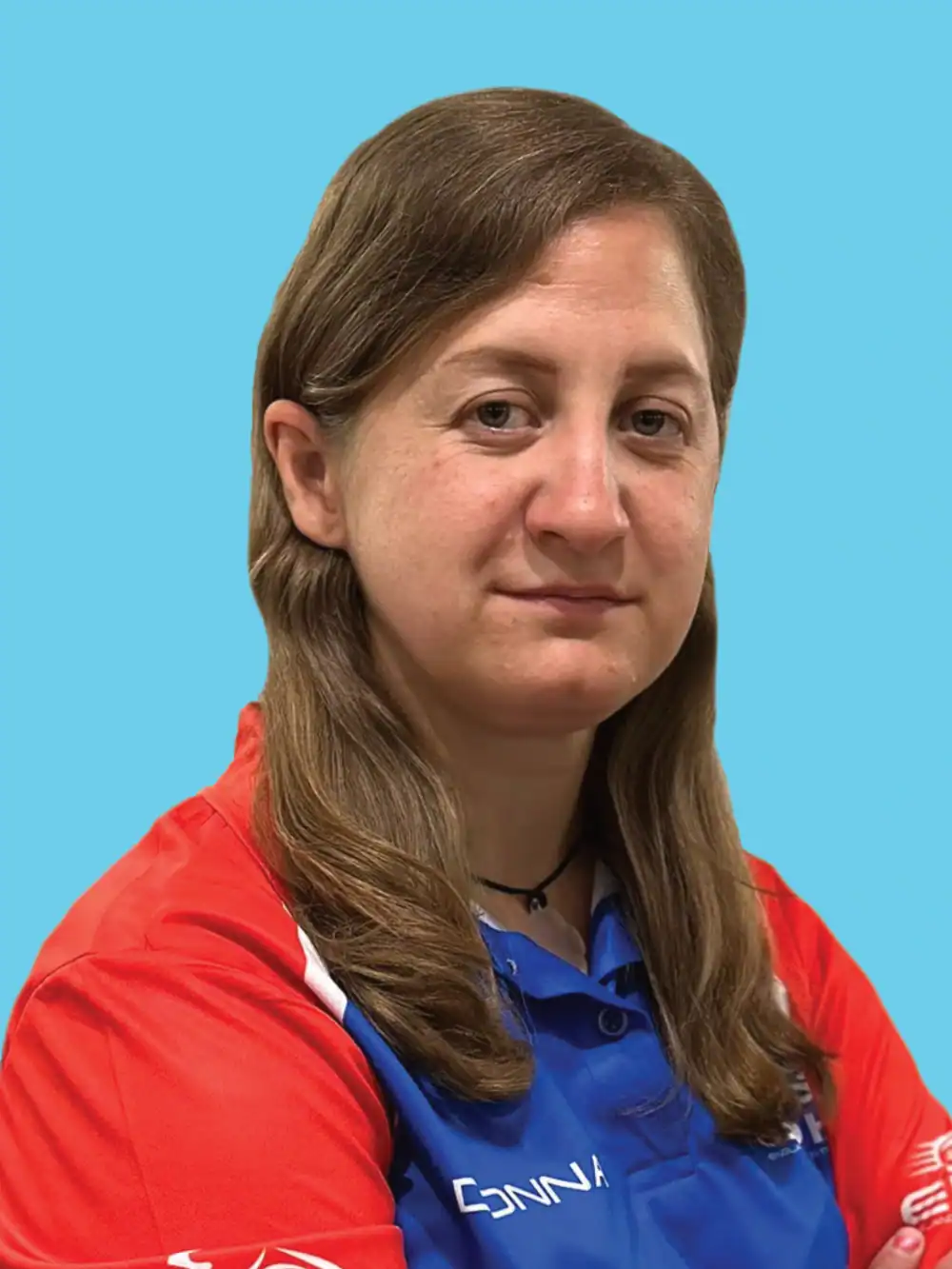 A person with long brown hair, wearing a red and blue collared sports shirt, poses against a solid light blue background.
