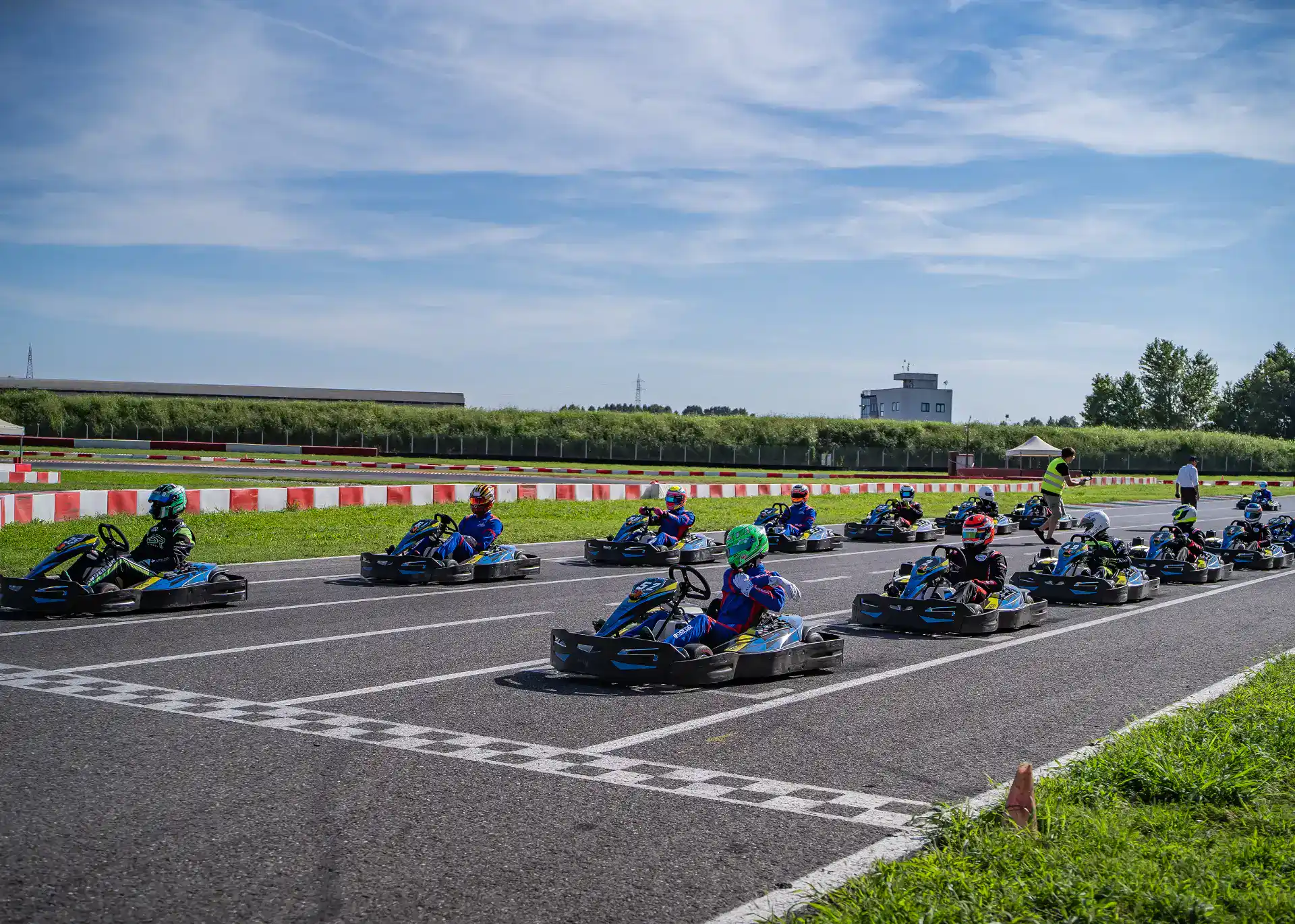 A group of people in go-karts lined up at the starting line on an outdoor race track, ready for a race on a sunny day.