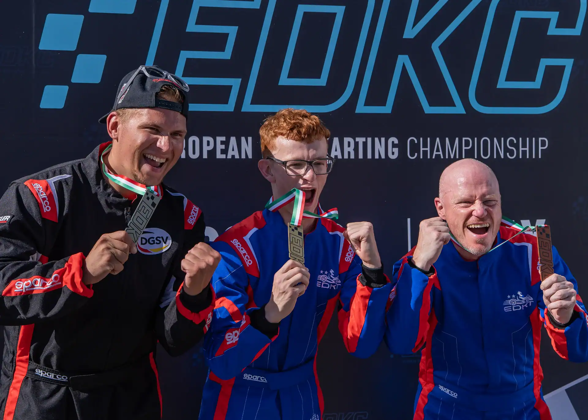 Three go-kart drivers in racing suits pose with medals in front of a European Karting Championship backdrop, celebrating their achievement.