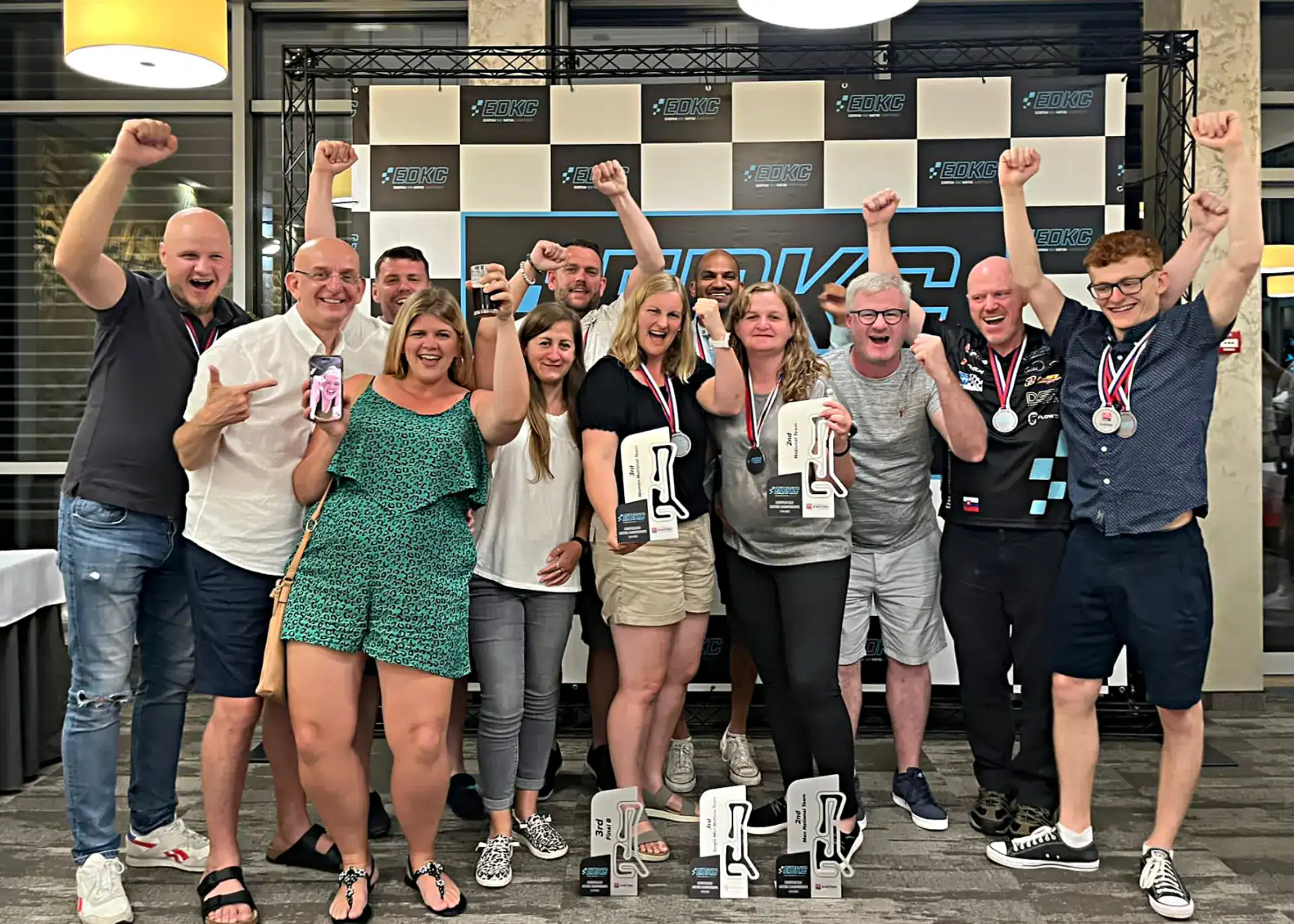 A group of people pose indoors, celebrating with trophies and medals, raising their arms in excitement in front of a sign that reads "RACE PARK.