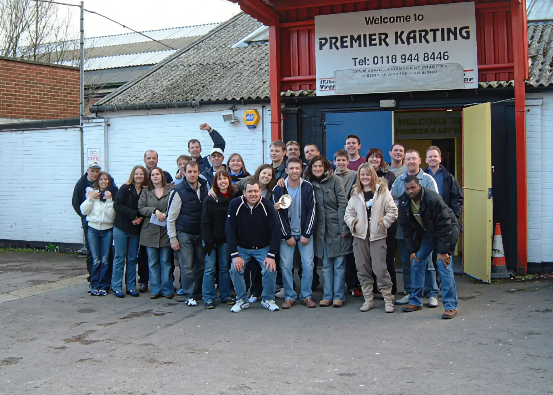 A group of people pose and smile for a photo outside a building with a sign that reads "Premier Karting".