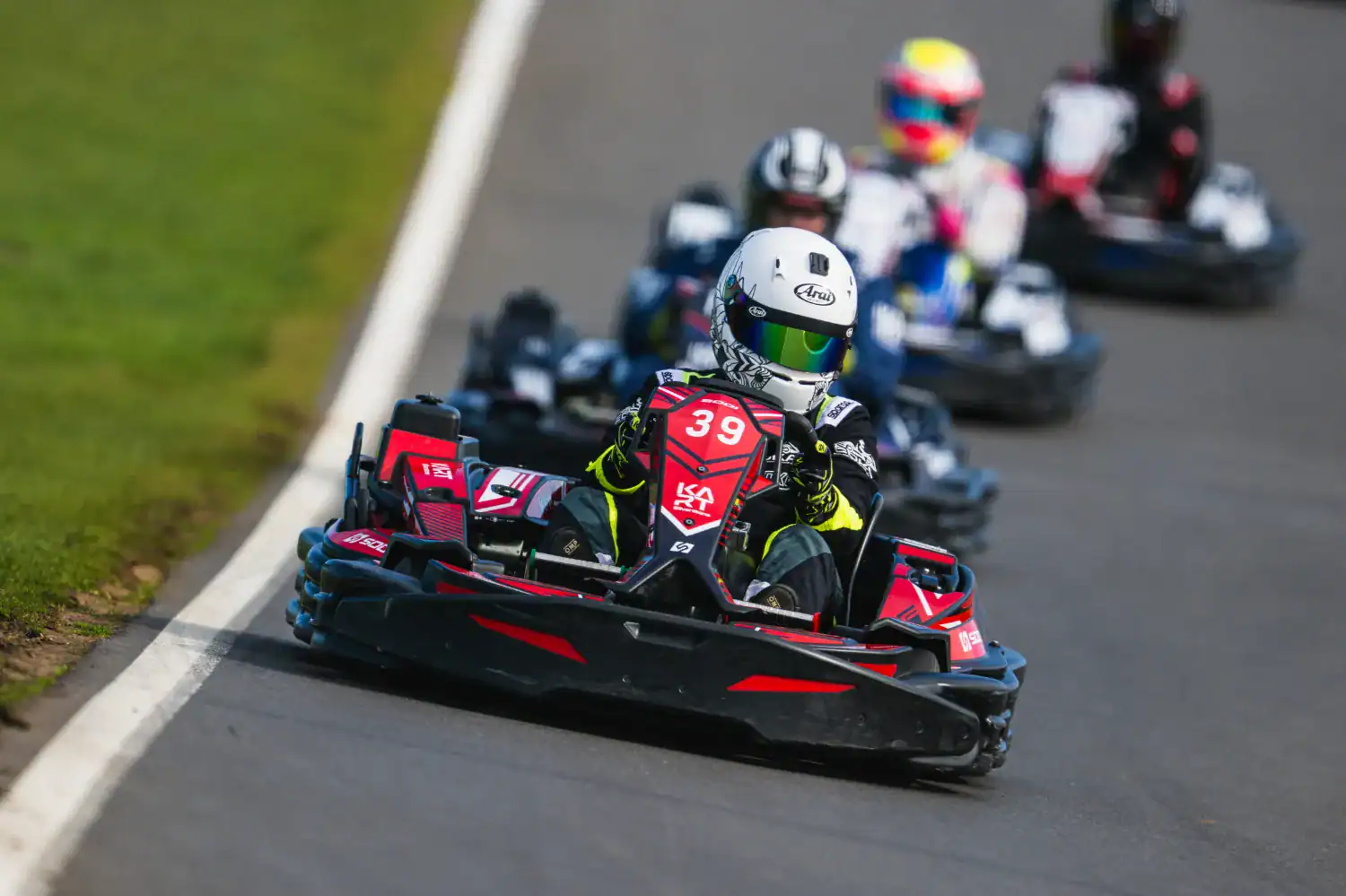Several go-karts race on a tarmac track, with the driver of kart number 39 in front, followed closely by others.
