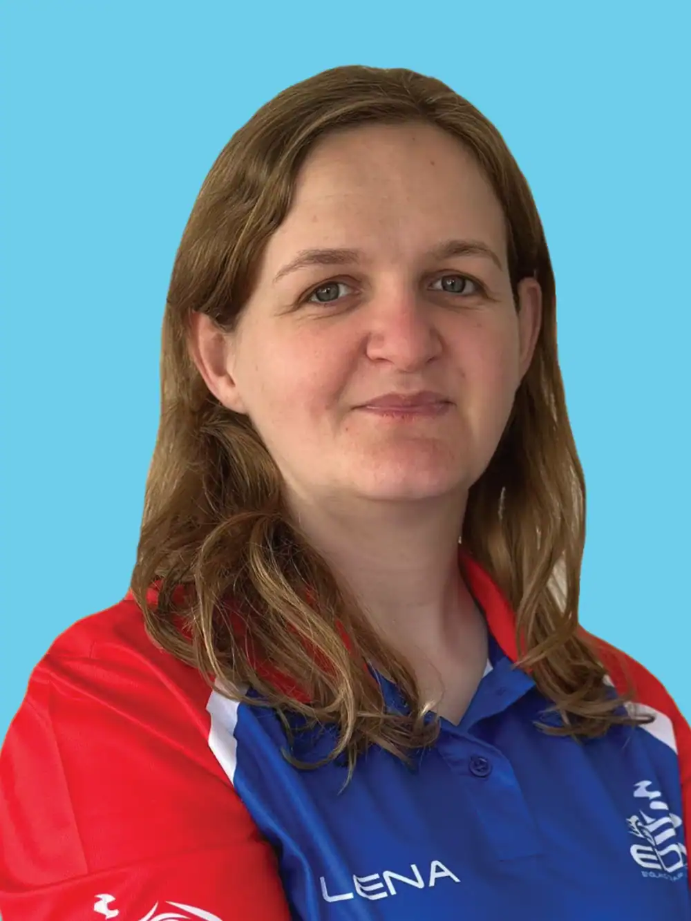 A woman with light brown hair wearing a blue and red collared shirt stands against a plain light blue background.