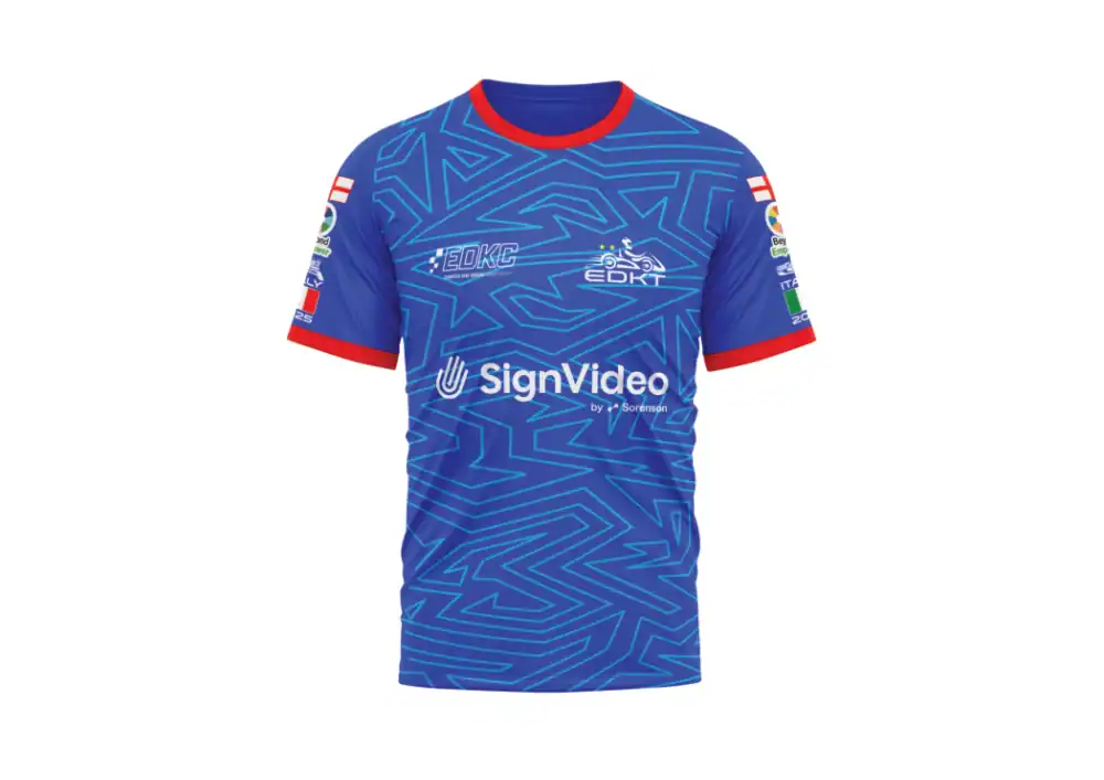A blue short-sleeve sports shirt with red collar and cuffs, geometric light blue patterns, and various sponsor logos on the chest and sleeves.